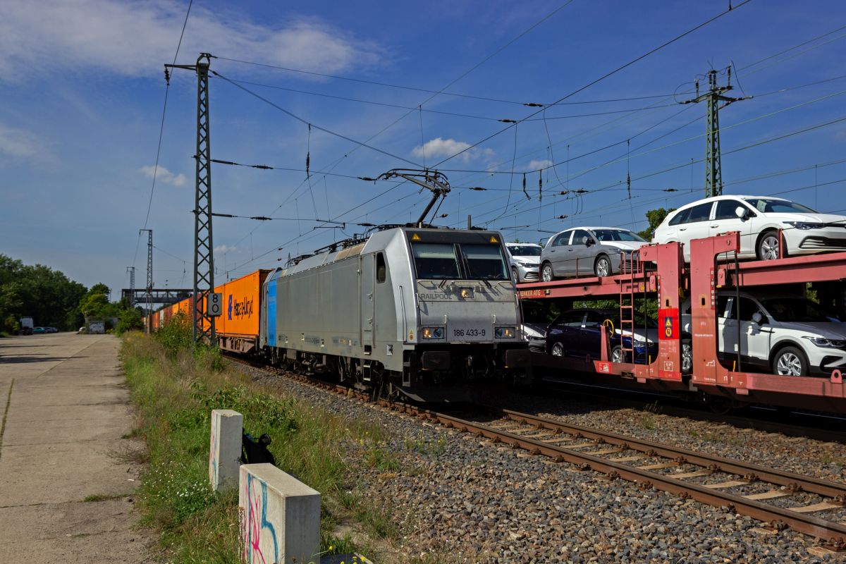 W�hrend ein Autotransportzug auf dem Durchfahrtsgleis in Saarmund einen Zwischenstopp einlegt, �berholt die Railpool-Lokomotive 186 433 mit einem Containerzug �ber das Bahnsteiggleis.