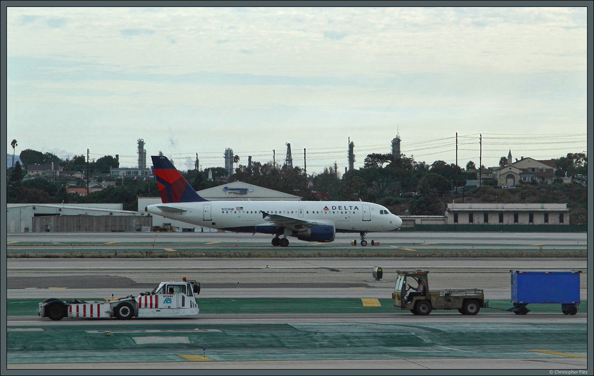 Während sich vorn zwei Flughafenfahrzeuge begegnen, rollt im Hindergrund der A319-114 N323NB der Delta Airlines zum Gate. (Los Angeles, 29.10.2016)